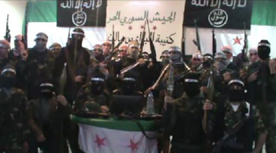 Capture from a video that shows Free Syrian Army soldiers with members of al-Qa'ida. In the background, alongside the banners of the Free Syrian Army, there are the familiar black flags of al Qaeda's Iraqi branch, with the black background and white Arabic script, featuring the Shahadah on top and a circular logo bearing the words "Allah, Rasul Mohammed." 
